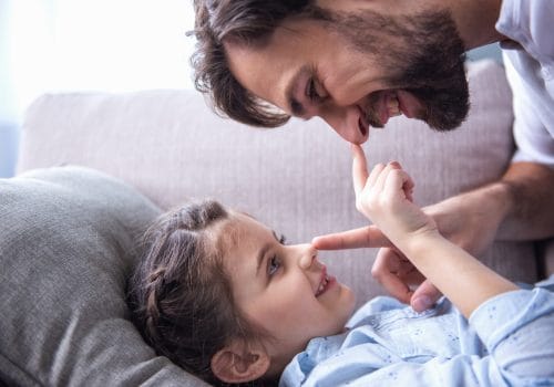 Cute little girl and her handsome father are hugging and playing together at home
