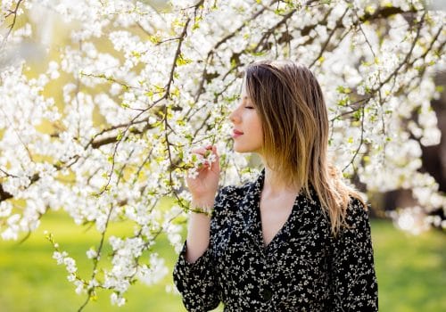 Young girl in dark dress stay near a flowering tree in the park. Spring season